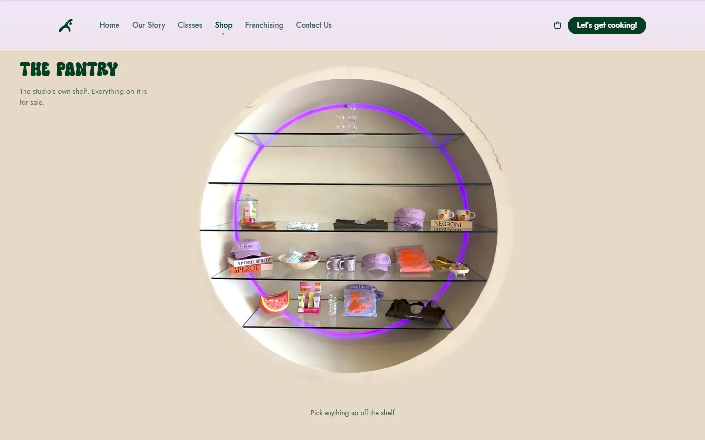 The Kitchen shop page, titled “The Pantry”: a round shelf lit in violet, holding caps, mugs and other studio merchandise